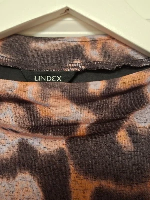 Långärmad blommig klänning från Lindex - Säljer en långärmad klänning från Lindex i storlek L. Klänningen har ett blommigt mönster i mörka och ljusa toner av lila, rosa och beige. Den är figurnära upptill och har en mjuk, stretchig känsla. Perfekt för dig som gillar unika prints och bekväma plagg.