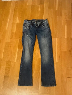 Blå bootcut jeans från LTB Valerie - Snygga blå jeans från LTB, modell Valerie, med bootcut-snitt och klassisk femficksdesign. Jeansen har slitningar och tvättade detaljer som ger en cool look. Materialet är jeans med dragkedja och knapp framtill. Perfekt för dig som gillar avslappnad stil.