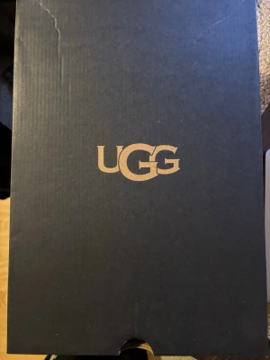 UGG Tasman Weather Hybrid Svart - UGG Tasman Weather Hybrid i svart med grov platt sula och rund tå. Skorna har en ovandel i mocka och syntet, samt vattentäta egenskaper. Insidan är fodrad med mjukt material och de har en justerbar snörning vid öppningen. Perfekt för kalla och blöta dagar.