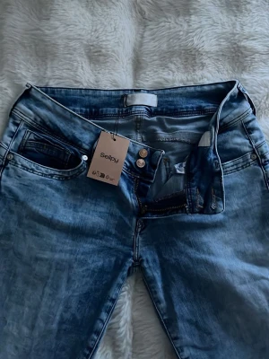 Ljusblå raka jeans med dubbla knappar - Säljer ett par ljusblå jeans med raka ben och dubbla knappar i midjan. Jeansen har klassisk femficksdesign och snygg tvättad look. Materialet är jeans och passformen är normal. 