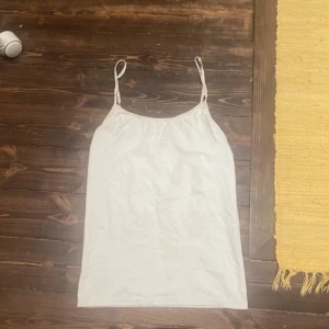 Vit enkel linnetopp med tunna band - Säljer en vit linnetopp med tunna axelband och rak passform. Toppen är ärmlös och har en minimalistisk look som passar perfekt till jeans eller kjol. Materialet känns mjukt och lätt, perfekt för varma dagar.