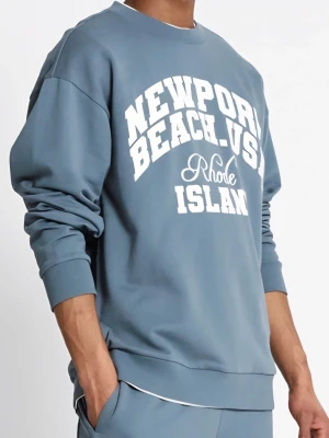 Blå Tröja Newport Beach  - Cool blå sweatshirt från Rhode Island med vit tryckt text 'Newport Beach USA' på bröstet. Tröjan har rund hals, långa ärmar och ribbade muddar vid ärmslut och nederkant. Perfekt för chill dagar och enkel att matcha med jeans eller mjukisbyxor. Printad sweatshirt i mjuk bomullskvalitet. Oversized passform med nerhasad axel. Ribb i hals, ärmslut och nederkant. Oborstad insida. Modellen är 183 cm lång och har på sig stl M. Nypris: 200 kr