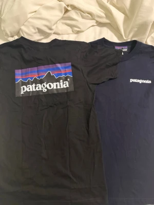 Patagonia t-shirt i svart, vit och marinblå - Säljer flera Patagonia t-shirts i svart, vit och marinblå. Alla har klassisk Patagonia-logga tryckt på bröstet, och en av de svarta har även ett stort färgglatt logotryck på ryggen. T-shirtsen är kortärmade och gjorda i mjuk bomull med rund hals. Perfekt för chill och streetwear.