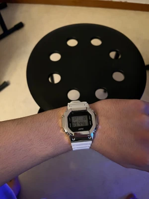 ATK Digital Klocka med Flerfärgad Bakgrundsbelysning - Modern digital klocka från ATK med vit rem och robust metallram. Utrustad med flera bakgrundsbelysningslägen (blå, grön, röd) och tydlig LCD-display. Funktioner som tidtagning, datum och larm. Klockan är i mycket gott skick utan synligt slitage.