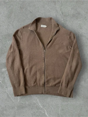 Beige ribbad kofta från East West | L - Säljer en beige ribbad kofta från East West i storlek XL. Koftan har hel dragkedja framtill, hög krage och långa ärmar. Materialet är stickat och ger en mjuk och skön känsla. Perfekt för lager-på-lager och chill stil.