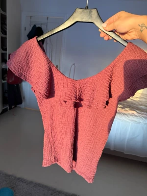 Vinröd omlott topp med volang från Lindex - Säljer en vinröd topp från Lindex i storlek S. Toppen har en omlott-design med bred volang längs den offshoulder ringningen och är tillverkad i ett krinklat syntetmaterial. Prislappen är fortfarande kvar då den aldrig kom till användning tyvärr!