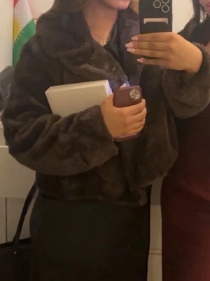 Mörkbrun pälsjacka med krage - Säljer en fluffig och mysig mörkbrun pälsjacka med bred krage. Jackan har en loose passform och är perfekt för dig som vill ha en varm och trendig look. Den har långa ärmar och är riktigt mjuk i materialet.