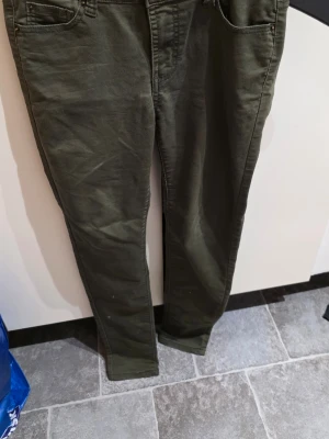 Mörkgröna jeans  - Snygga jeans klassisk femficksdesign. Byxorna är tillverkade i en mjuk och stretchig mix av bomull, polyester och elastan, vilket gör dem riktigt sköna att ha på sig. Perfekta för dig som gillar en stilren look med lite edge.