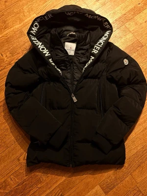 Svart Moncler pufferjacka - | INTRESSEKOLL, LÄGG BUD |                                       Säljer en svart pufferjacka från moncler. Jag är inte 100% säker på om den är äkta eller ej men QR-koden går att skanna.. den är varm om man kan lita på den i Sveriges kyla. Bara att höra av sig vid frågor!