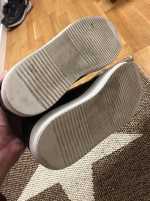 Svarta sneakers från Sandays - Snygga svarta sneakers från Sandays med blank tå och vit platt sula. Skorna har snörning och en stilren design som passar till många olika outfits. Materialet är en mix av skinn och syntet, vilket ger en cool kontrast mellan matt och blank yta.