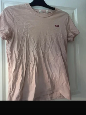 Ljusrosa Levi's t-shirt  - Säljer en ljusrosa t-shirt från Levi's i storlek S. T-shirten har klassisk rund hals, korta ärmar och en liten röd Levi's-logga på bröstet. 