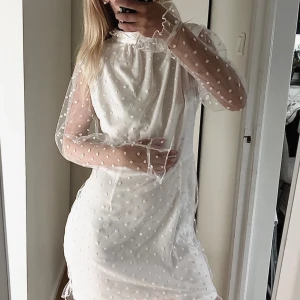 Vit prickig kortklänning från Parisian - Supersöt vit kortklänning från Parisian med transparenta långärmar och prickigt mönster. Klänningen har hög hals och volangdetaljer vid ärmslut. Materialet är lätt och ger en romantisk vibe, perfekt för dig som gillar unika detaljer. Storlek 40 men passa nog M/l