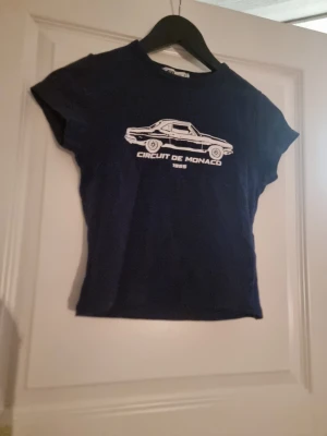 Mörkblå Circuit de Monaco t-shirt - Snygg mörkblå t-shirt med vit bil och texten 'Circuit de Monaco 1955' tryckt på bröstet. T-shirten har korta ärmar och en klassisk passform. Perfekt för dig som gillar motorsport och retrostil.