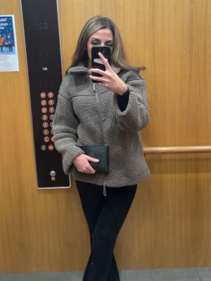 Beige teddyjacka med dragkedja - Mysig beige teddyjacka med hög krage och hel dragkedja framtill. Jackan har en avslappnad passform och är tillverkad i mjukt fleece-liknande material som håller dig varm. Perfekt för kyliga dagar och enkel att styla med dina favoritjeans eller mjukisbyxor. XXS