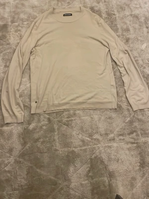 Beige stickad tröja från Zadig & Voltaire - Snygg beige stickad tröja från Zadig & Voltaire med rund hals och lång ärm. Tröjan har en diskret metallknapp med logga vid nederkanten och är i mjukt material som känns skönt mot huden. Perfekt för lager-på-lager under hösten och vintern. Fits M skulle jag säga med ett 9/10 skick 