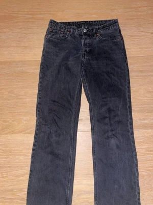 Svarta Weekday Pin jeans W27 L30 - Säljer ett par svarta Weekday Pin jeans med klassisk femficksdesign och raka ben. Jeansen har mid midja och är tillverkade i ett mjukt denimtyg. Passformen är raka och färgen är tvättad svart för en cool look.