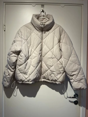 Vitgrå quiltad jacka - Superfin och go vit-grå jacka från H&M, Divided. Den är lite tunnare än en ”klassisk pufferjacket” och passar bra till höst/vår eller lite varmare dagar på vintern 🤍 Jackan är i väldigt fint skick! Den har fickor och kan dras åt i nederkant, se bild 🥰