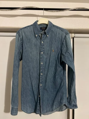Ralph Lauren jeansskjorta - En Jeansskjorta från Ralph Lauren som har ett lite mjukare tyg. Skjorta är i bra skick då jag inte använd den så mycket eftersom att den är för lite för mig. Nypris 1600.
