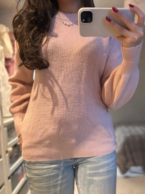 Ljusrosa stickad tröja - Säljer en ljusrosa stickad tröja med rund hals och långa ärmar. Tröjan har en ribbad struktur och en avslappnad passform som är perfekt för chill dagar. Enkel och stilren design som funkar till jeans eller kjol.