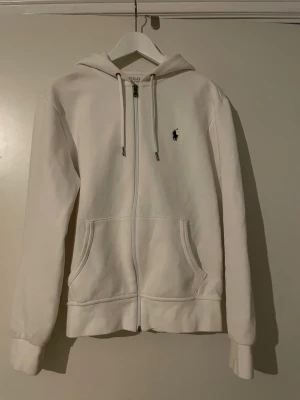 Vit Ralph Lauren fullzip  - Vit Ralph Lauren fullzip med svart broderad logga på bröstet. Använd ett fåtal gånger och passar dig som vill ha något stilrent och bekvämt😁