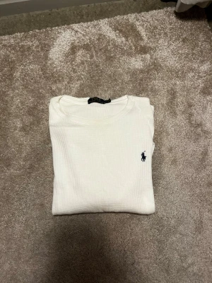 Vit långärmad tröja från Polo Ralph Lauren - Vit långärmad tröja från Polo Ralph Lauren med klassisk blå broderad logga på bröstet.  OANVÄND  Tröjan har en ribbad rund hals och är tillverkad i ett strukturerat bomullsmaterial som ger en skön och avslappnad känsla. Tröjan är storlek L men sitter lite mer som en M Perfekt för dig som gillar stilrena och tidlösa plagg. Priset ej huggget i sten hör av er vid frågor eller funderingar! 