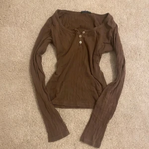Brun ribbad långärmad topp  - Brun långärmad topp från Brandy Melville med tre knappar framtill. Säljs inte i Sverige längre