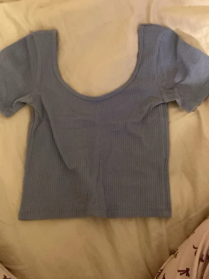 Ljusblå ribbad croppad topp - Säljer en ljusblå croppad topp med ribbad struktur och djup rundad halsringning. Toppen har korta ärmar och är tillverkad i ett mjukt och stretchigt material som sitter snyggt på kroppen. Perfekt att matcha med jeans eller kjol. Okänt märke men tror den är från VeroModa och storlek xs/s