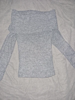 Grå offshoulder tröja  - (PRIS KAN DISKUTERAS) Säljer en grå stickad offshoulder-tröja från H&M i storlek XS. Tröjan har lång ärm och bred krage som kan bäras ned över axlarna. Mjuk och skön kvalitet, perfekt för kyliga dagar. Den sitter ganska tight och fint runt kroppen. Den kliar inte på huden! Passar dig som gillar stilren och enkel look.