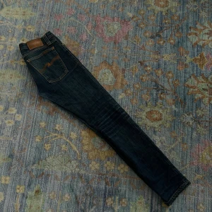 Nudie Jeans - Säljer ett par  jeans från Nudie. Jeans med klassisk orange söm och snygg broderad detalj på bakfickan. Jeansen har fem fickor, och är tillverkade i slitstarkt jeansmaterial. Perfekt för dig som gillar en smal passform och stilren look.