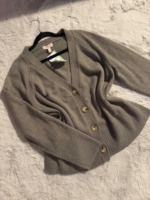 Mysig stickad kofta  - Snygg och mysig kofta från H&M med v-ringad hals och fyra stora knappar framtill. Modellen har långa ärmar och breda ribbade muddar vid ärmslut och nederkant. Perfekt att slänga på sig när det är lite kyligt ute. Helt ny! Passar S/M då den är oversized 