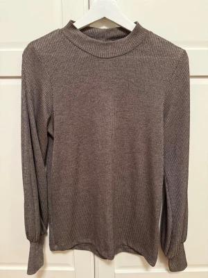 Ribbad brun långärmad tröja/topp - Brun ribbad tröja från CC i storlek S. Tröjan har en hög krage och är tillverkad i ett mjukt stickat material. Den har en enkel och stilren design med långa ärmar och en rak passform. 
