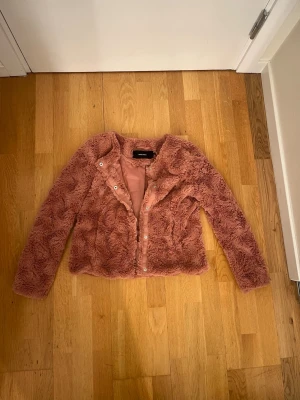 Rosa teddyjacka från Vero Moda - Fluffig teddyjacka i en snygg rosa ton från Vero Moda. Jackan har långärmade ärmar, stängs med knappar framtill. Perfekt för dig som gillar mjuka och trendiga plagg med cozy vibe.