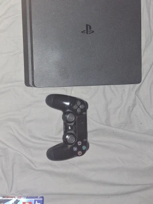 PlayStation 4 med handkontroll och 5 spel - Säljer en PlayStation 4 i gott skick med original handkontroll som är lite sönder går när man siktar och fem populära spel: GTA V, Mafia III, Uncharted 4, Overwatch och LEGO Ninjago Movie. Konsolen och kontrollen har mindre yttre slitage men fungerar utmärkt. Perfekt för dig som vill ha en komplett spelupplevelse direkt! 