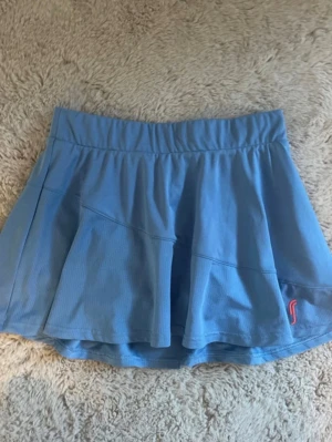 Blå sportkjol från RS Sports - Säljer en ljusblå kortkjol från RS Sports i storlek 12-14 Junior. Kjolen är tillverkad i 100% polyester och har inbyggda shorts under för extra komfort. Perfekt för tennis eller andra sportaktiviteter. Enkel design med elastisk midja och liten logga framtill.