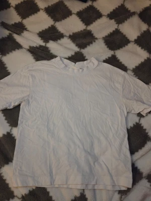 Vit basic t-shirt från Gina Tricot XS - En klassisk vit t-shirt från Gina Tricot, basically basics-kollektionen. Modellen är kortärmad med rund hals och tillverkad i 100% ekologisk bomull. Perfekt att styla med jeans eller under en hoodie för en chill look.