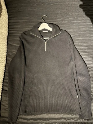 Svart ribbad half zip stickad tröja Jack & Jones - Säljer en svart stickad tröja från Jack & Jones med ribbad struktur och half zip-dragkedja vid kragen. Tröjan har lång ärm och en loose passform som gör den chill och enkel att styla. Perfekt för lager-på-lager under höst och vinter.