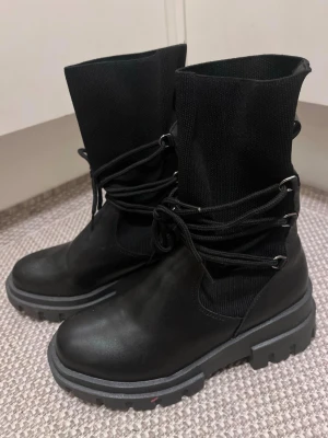 Svarta chunky boots  - Svarta chucken boots med grov sula och snörning runt skaftet. Ovandelen är i en kombination av skinn och stickat syntet material, som en strumphals. Riktigt snygga med strumpbyxor eller leggings! Storlek 37. Mycket bra skick! 
