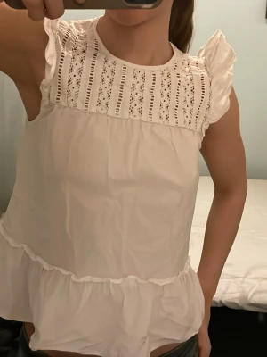 Vit blus med spets och volang - Säljer en söt vit blus med spetsdetaljer upptill och volang nedtill. Jätte söt både sommar o vintertopp. Passar vi lite finare tillställningar eller med en kofta över nu till vintern. Söt topp från Hm i xs