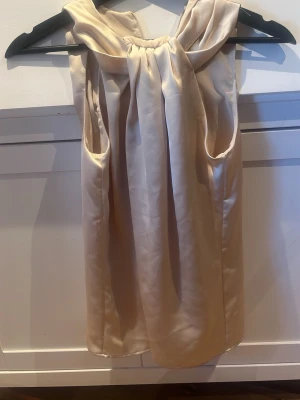 Champagnefärgad blus H&M XS - Säljer en elegant blus i fint skick. Champagnefärgad satin-look. Blusen är ärmlös med en snygg rosettdetalj vid halsen och har dragkedja i ryggen. Köpte secondhand. Den är tyvärr liten för mig därför säljer jag. 💕Buda gärna och skriv om ni har några frågor! 