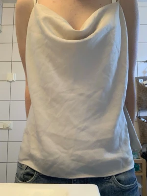 Luftig och snygg topp från River Island - Säljer en stilren topp från River Island i storlek 12. Toppen har tunna axelband och en snygg draperad halsringning. Materialet är mjukt och har en lätt glansig finish som ger en lyxig känsla. Jag har storlek S och då är den luftig och sitter lösare så är nog storlek M egentligen. Pris kan gå att diskutera.