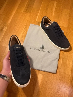Brunello Cucinelli - Snygga mörkblå sneakers från Brunello Cucinelli i mjuk mocka med vita platta högkvalitativa sulor. Skorna har rund tå, klassisk snörning och beige innersida i skinn. Perfekta för dig som gillar stilrena och lyxiga sneakers med premiumkänsla. Riktigt unik piece för dig som letar efter något speciellt att sticka ut med! 🏎️