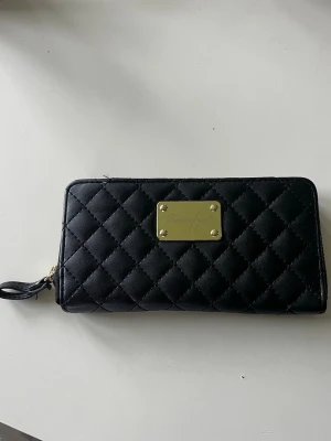 Svart quiltad plånbok - Snygg svart plånbok med quiltat mönster och guldfärgad metallplatta. Perfekt storlek för kort, kontanter och mobilen🥰 