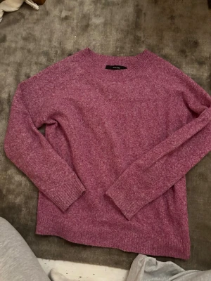 Rosa stickad tröja från Vero Moda - Mysig rosa stickad tröja från Vero Moda i storlek M. Tröjan har en rund halsringning, ribbade muddar vid ärmslut och nederkant samt långärmad passform. Perfekt för kyliga dagar och enkel att matcha med jeans eller kjol.