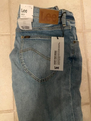 Ljusblåa Lee jeans - Säljer ett par ljusblå jeans från Lee i relaxed fit med klassisk femficksdesign och Lee-logga på bakfickan. Jeansen har normal passform, raka ben och är tillverkade i bomull. Snygga slitningar framtill och vintagekänsla. Perfekta för dig som gillar avslappnad stil.