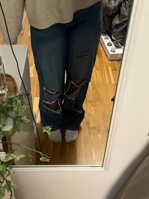 Blå ripped jeans från Boohoo - Säljer ett par blå jeans från Boohoo med stora slitningar och hål på båda benen. Jeansen har en rak passform och är tillverkade i klassiskt denimtyg. Perfekta för dig som gillar en avslappnad och edgy stil.