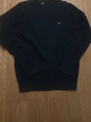 Mörkblå ribbad tröja från GANT - Säljer en mörkblå ribbad tröja från GANT i storlek S. Tröjan har rund halsringning, diskret GANT-logga med sköld på bröstet och långa ärmar. Perfekt för dig som gillar klassisk och stilren look.