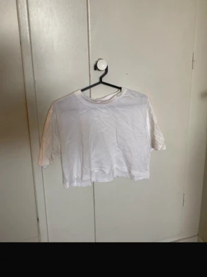 Vit croppad t-shirt från Zara - En basic vit croppad t-shirt från Zara i mjuk bomullsmix med lite stretch. T-shirten har korta ärmar och en klassisk rund halsringning. Perfekt till jeans eller kjol för en clean och enkel look. Kolla gärna in min profil då jag säljer massor av kläder superbilligt! Tveka inte att höra av dig om du har frågor💕