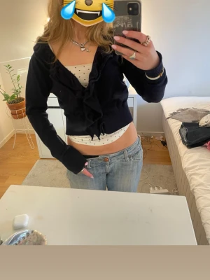 Mörkblå volangkofta Flash Essential - Supersöt mörkblå kofta från Flash Essential med volangdetaljer framtill. Koftan är croppad och har lång ärm, perfekt att slänga över ett linne eller topp. Mjuk och skön stickad känsla, passar till jeans eller kjol.