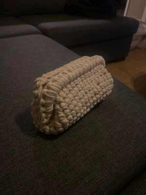 Beige stickad kuvertväska - Handgjord beige kuvertväska i grovt stickat material. Väskan har en mjuk och chunky känsla med tydlig struktur och öppningsbar topp. Perfekt accessoar för dig som gillar unika detaljer och en mysig stil.