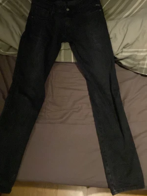 Replay svarta jeansbyxor straight fit - Svarta jeansbyxor från Replay med klassisk femficksdesign och subtila slitningar. Modellen har rak passform och normal midja, med snygga detaljer vid fickorna och knappstängning framtill. Perfekt för dig som gillar stilrena och tidlösa jeans. Köpta på jeansbolaget, kvitto medföljer 